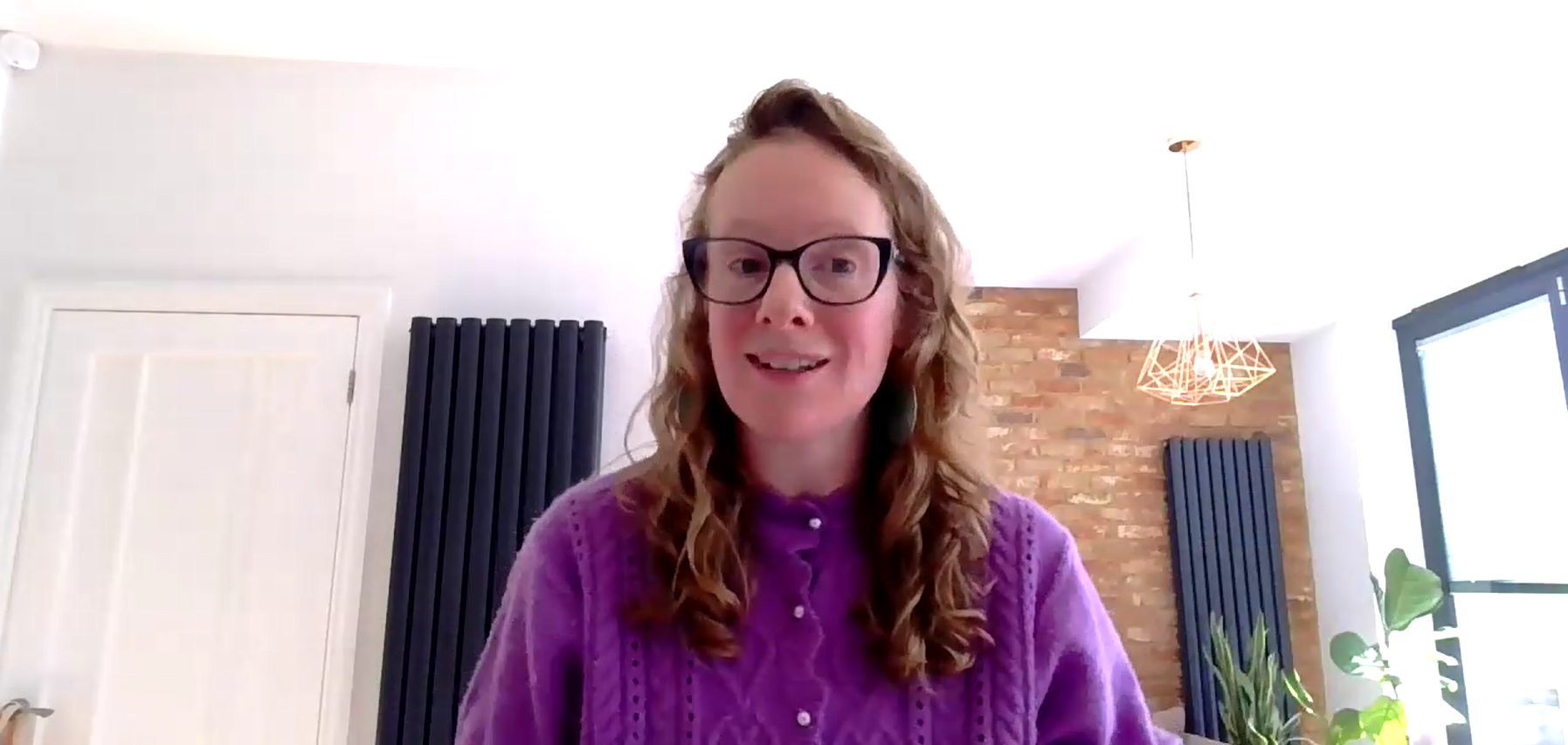 Screenshot of Jess Meredith speaking during the webinar. Jess has long red curly hair and is wearing a purple cardigan and glasses.