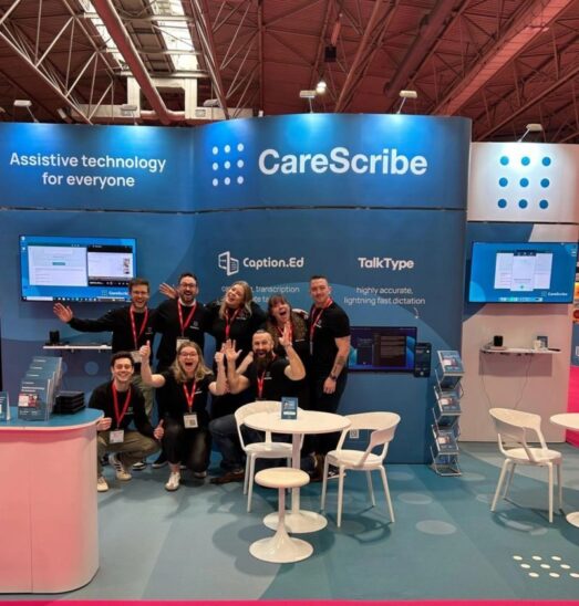 The CareScribe team at an event surrounded by branded banners, merchandise and TV screens for demos. They are facing the camera smiling and looking very happy and silly.