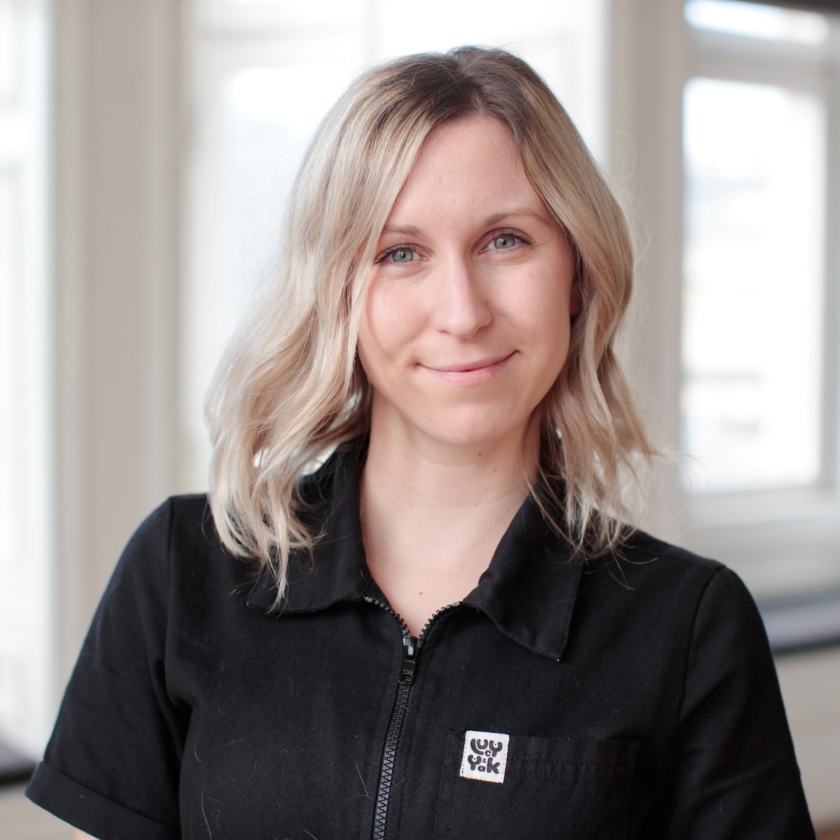 Claire is in a white office environment with shoulder length blonde hair and wearing a black top.